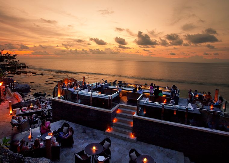 Bali cliffside rock bar at sunset with tiered candlelit terraces overlooking the ocean