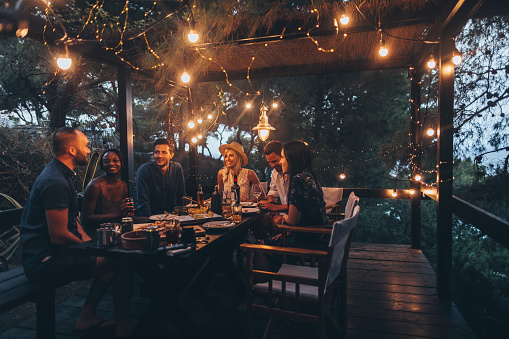An intimate group of six sharing an evening dinner under warm string lights on a rustic terrace